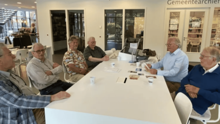 Vrijwilligers van het ZHG zitten aan een grote witte tafel in de publiekshal van het gemeentehuis.