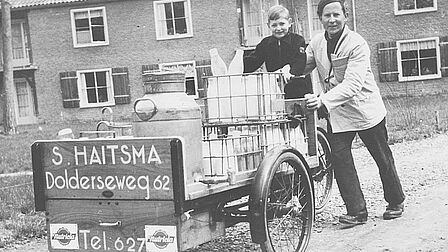 Man en kind bij een bakfiets vol melk. 